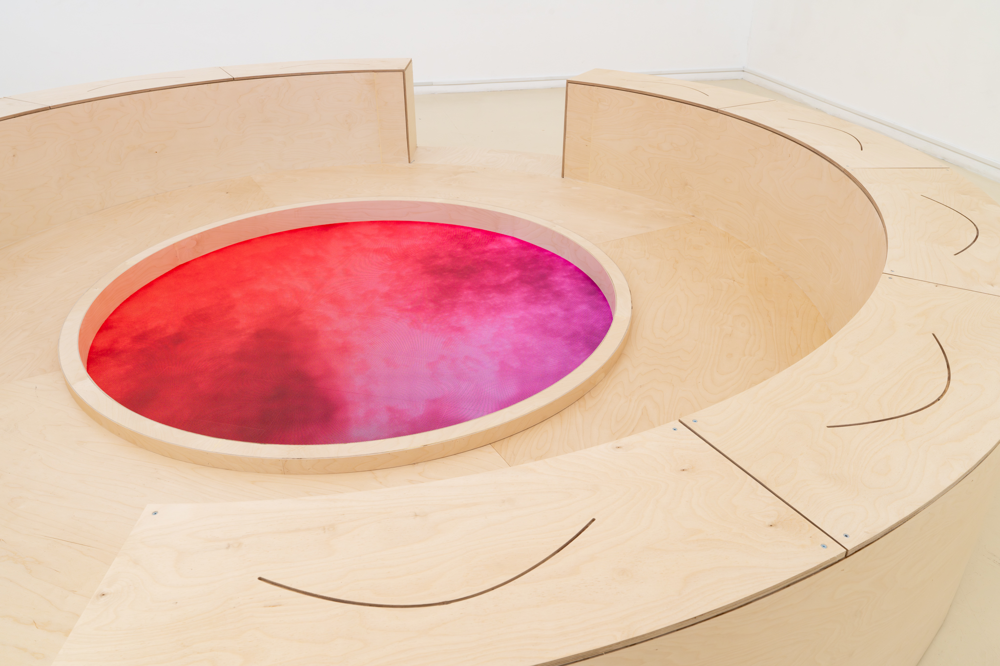 Detail of the round floor screen glowing red to magenta inside the plywood ring