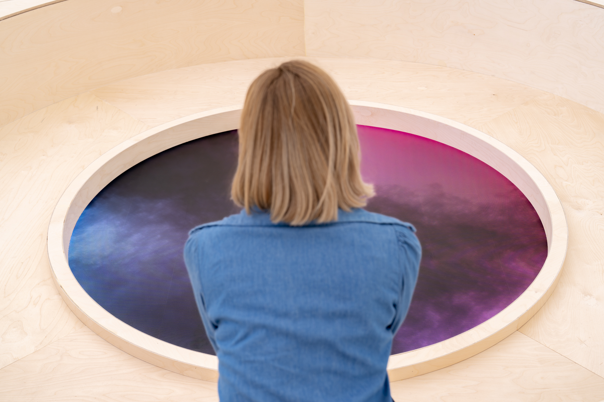 A visitor seen from behind, looking down at the floor screen as it shifts to blue and purple